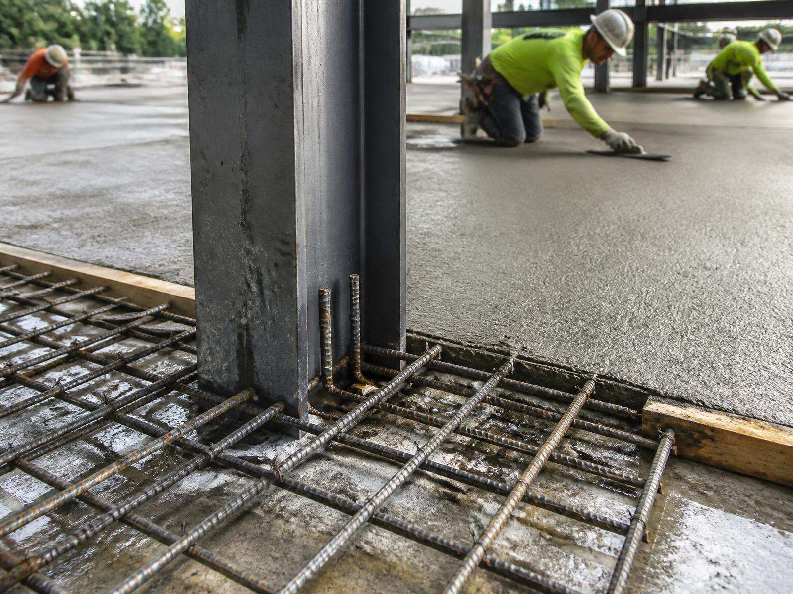 Reinforcing steel and freshly placed concrete slab being finished by a crew